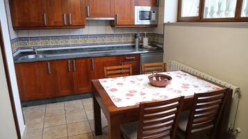 Una cocina con armarios de madera, microondas, pileta y una mesa de comedor con sillas.