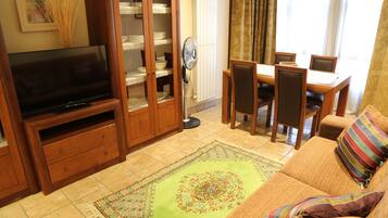 A living room with a TV, wooden cabinet, dining table, chairs, and a sofa.