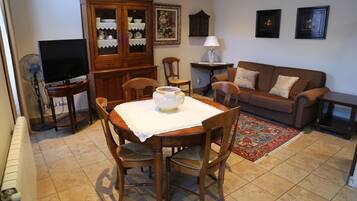 A dining area with a table set for four, surrounded by wooden chairs. A television is placed on a stand to the left.