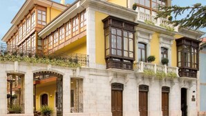 A multi-story building with a yellow facade, large windows, and a balcony with a wrought iron railing. - La Pontiga (Pilona)