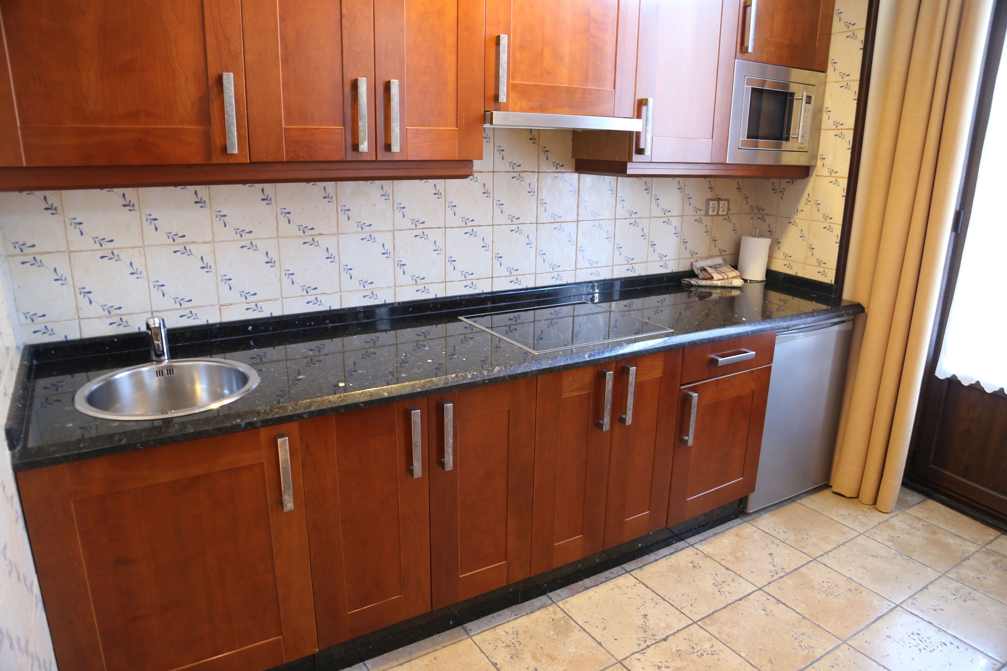 Una cocina con armarios de madera, un lavamanos de acero inoxidable, un microondas y un salpicadero de azulejos.