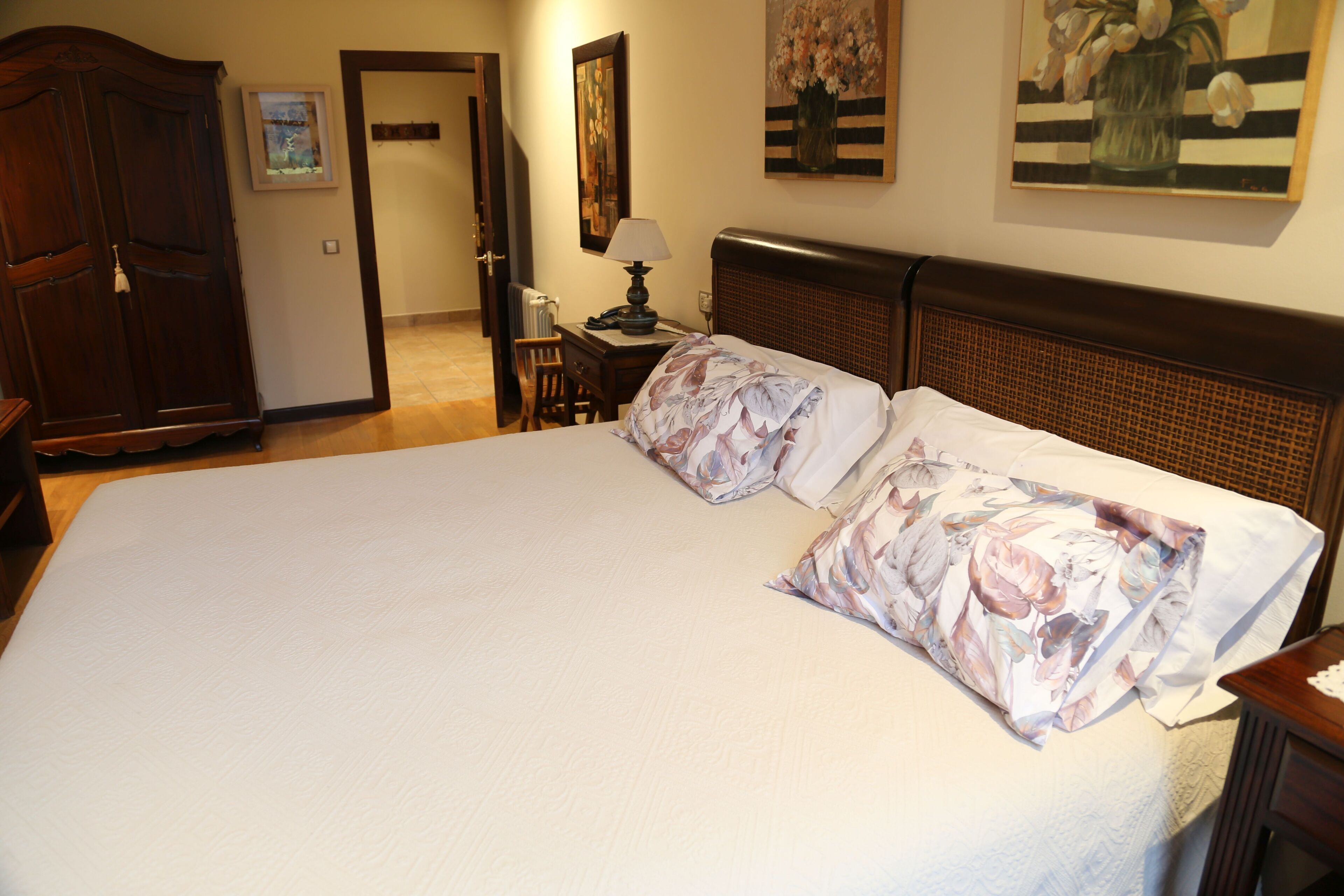 Una cama grande con ropa de cama floral, una mesita de noche con lámpara y un armario de madera.