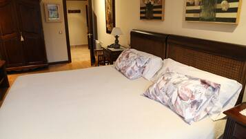 Una cama grande con ropa de cama floral, una mesita de noche con lámpara y un armario de madera.