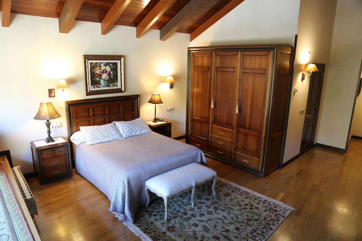 Un dormitorio con cama, mesitas de noche, un banco, un armario y lámparas de pared.