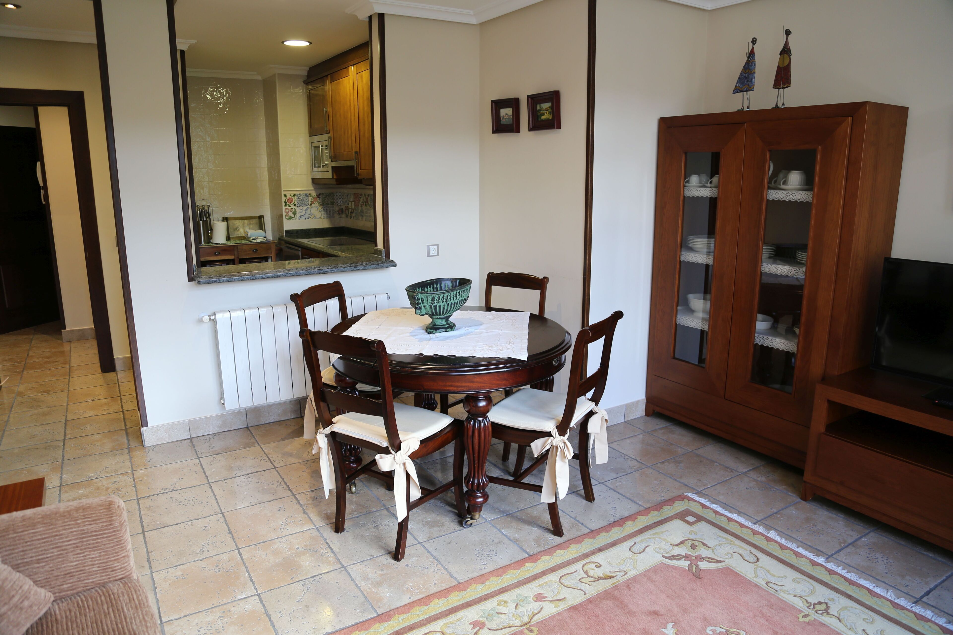 Een eetgedeelte met een ronde tafel, stoelen, een grote spiegel en een kast met glazen deuren.
