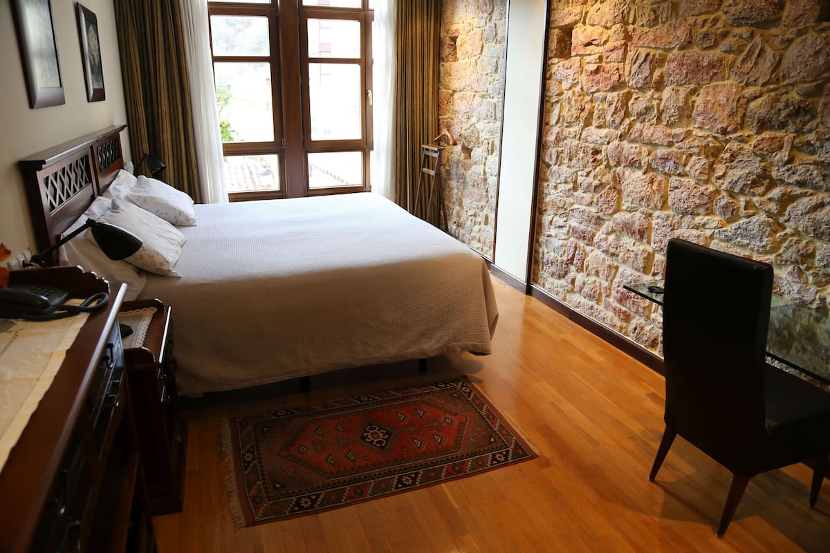 Un dormitorio con cama, escritorio de madera, silla y pared de piedra.