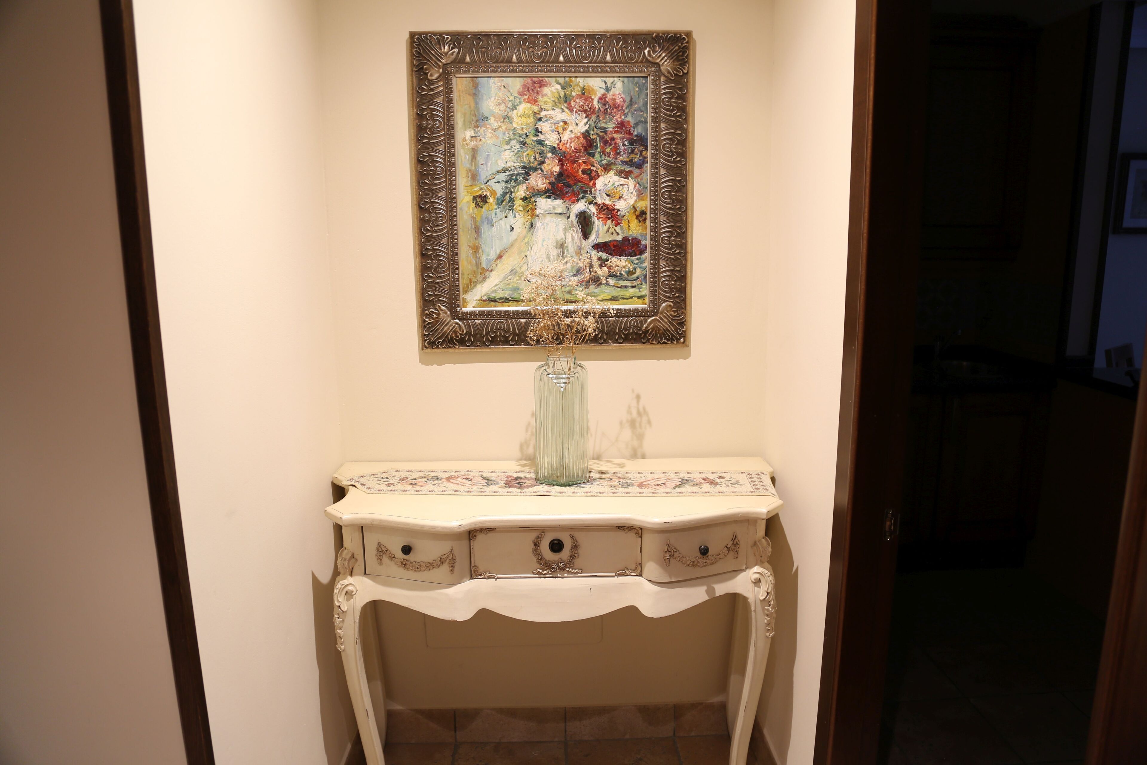 A hallway with a white console table, a framed painting, and a vase.