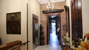 A hallway with a brick wall, a chandelier, a wooden door, and a framed painting. - La Pontiga (Pilona)
