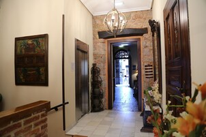 Un pasillo con pared de ladrillo, un candelabro, una puerta de madera y un cuadro enmarcado.