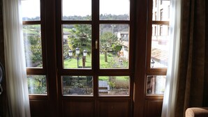 A view through a wooden door with multiple windows, revealing a garden with various plants and a building in the background. - La Pontiga (Pilona)