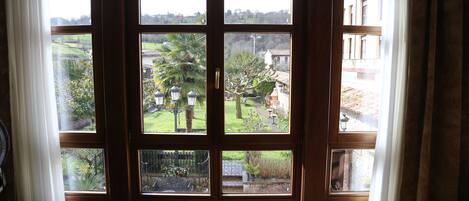 A view through a wooden door with multiple windows, revealing a garden with various plants and a building in the background.
