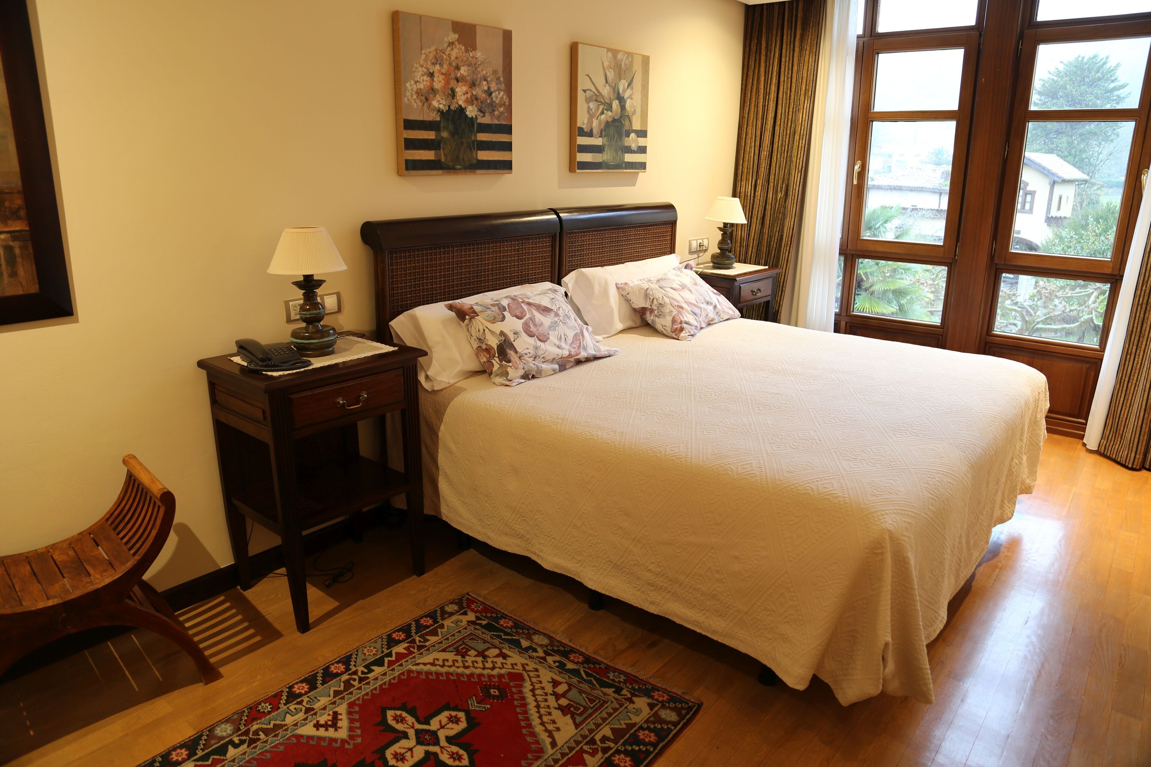 A neatly arranged bedroom with a large bed, two bedside tables with lamps, a wooden bench, and a patterned rug.