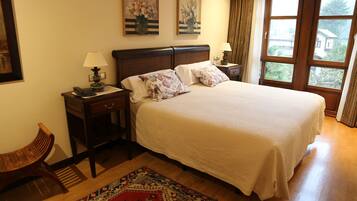 A neatly arranged bedroom with a large bed, two bedside tables with lamps, a wooden bench, and a patterned rug.