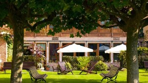 A courtyard with two lounge chairs, a white umbrella, and a brick building with large windows. - La Pontiga (Pilona)