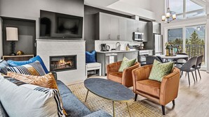 A modern living room with a fireplace, sofas, and a dining area with a view. - Delightful 3BR Condo w/ AC+Stunning Mountain Views (Canmore)