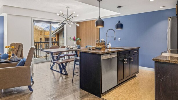 Une cuisine moderne dotée d’un îlot central, de meubles de rangement aux couleurs sombres et d’un éclairage suspendu.