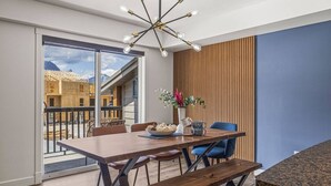 Un espace de salle à manger moderne avec une table en bois, des chaises bleues et un banc. Un lustre à plusieurs ampoules est suspendu au-dessus.