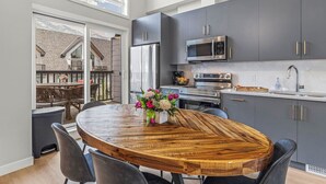 Een moderne keuken met grijze kastjes, roestvrijstalen apparatuur en een houten eettafel met stoelen.