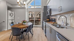 Een moderne keuken met roestvrijstalen apparatuur, een houten eettafel en uitzicht op een balkon.