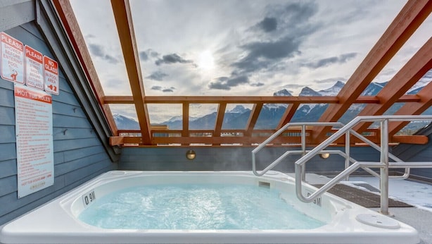 Een hottub met uitzicht op bergen, omringd door houten leuningen en een bewolkte lucht.