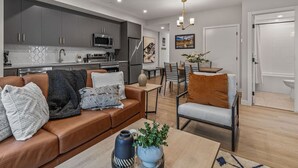 Una sala de estar moderna con un sofá de cuero marrón, una mesa de centro con un florero y una planta, y un comedor con una mesa y sillas.