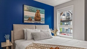 Un dormitorio con una cama grande, vistas de un edificio a través de una ventana y un cuadro de osos en la pared.
