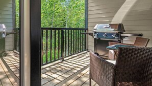 Un patio techado al aire libre con una parrilla, sillas de mimbre y vistas a árboles.