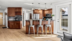 Una cocina moderna con gabinetes de madera, una isla central con taburetes de bar, electrodomésticos de acero inoxidable e iluminación colgante.