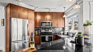 Una cocina moderna con armarios de madera, electrodomésticos de acero inoxidable, una encimera de mármol y un ventanal grande.