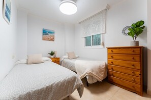A bedroom with two beds, a wooden dresser, a window with a view, and a beach-themed painting on the wall. - MalagaSuite El Levante Apartment 1 (Torremolinos)