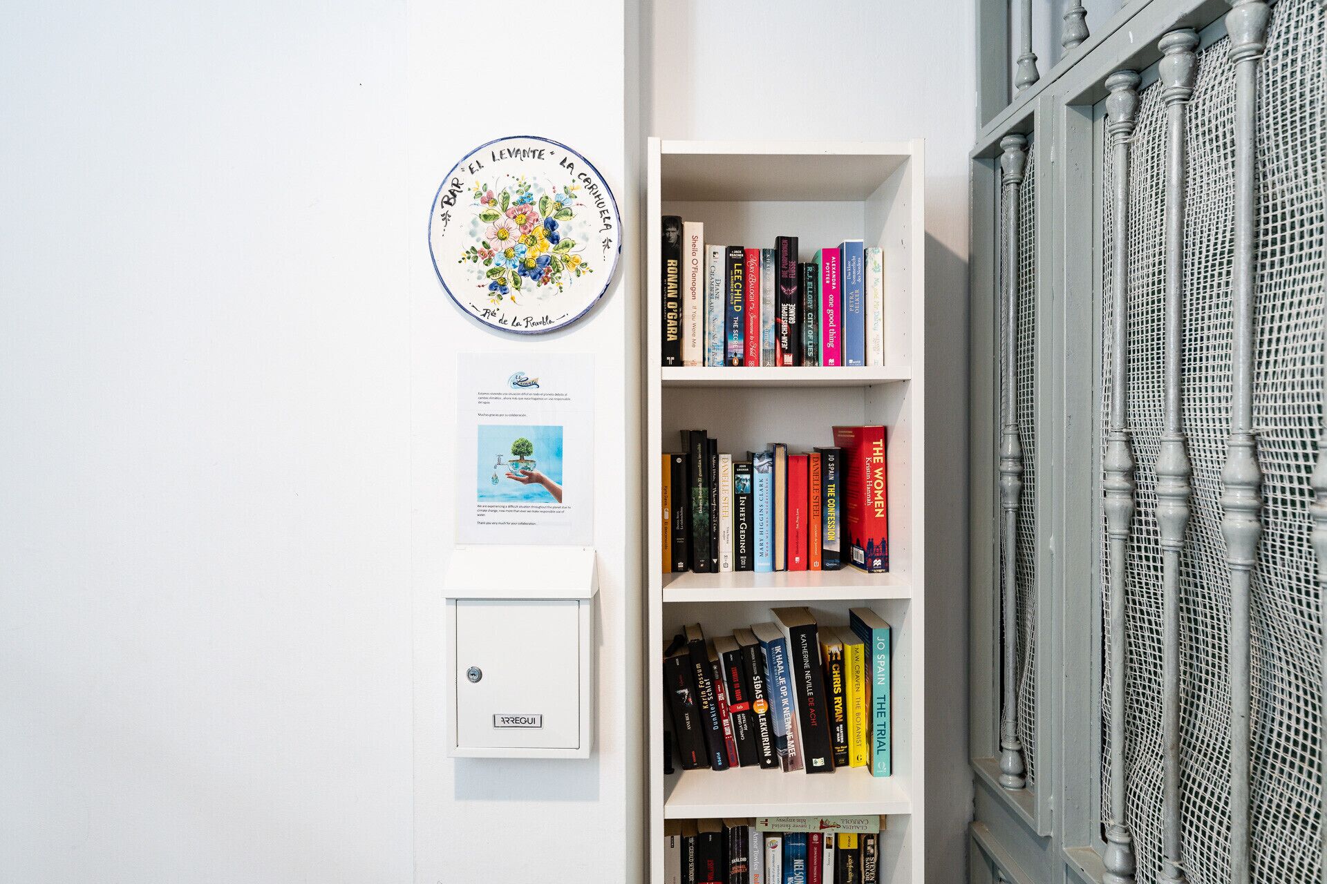 Een boekenplank met verschillende boeken, een rond decoratief bord en een klein bordje aan de muur.