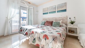 Un dormitorio con cama, mesita de noche, planta en maceta y vistas al exterior.