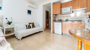 Un espacio habitable compacto con kitchenette, un sofá, una pequeña mesa de comedor y una cama.