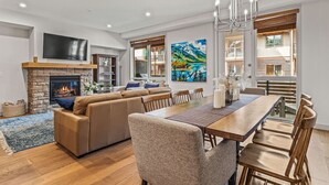 Een moderne woonkamer met een open haard, een ruime bank, een eettafel en uitzicht op de omgeving.