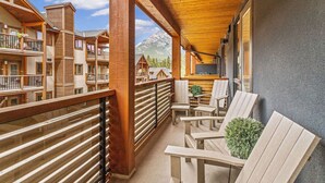 Een houten balkon met stoelen en een kleine tafel, met uitzicht op een bergachtig landschap.