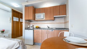 Cocina compacta con armarios de madera, microondas y refrigerador. Cuenta con una mesa de comedor, platos y una silla.