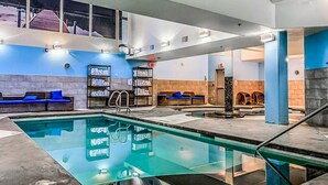 An indoor swimming pool with blue and white walls, a tiled floor, and a ceiling with exposed beams. There are lounge chairs and a shelf with towels. - Superb 2BR Condo w/ Charming Mountain View & Pool (Canmore)