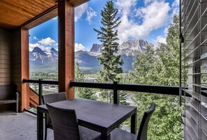 A balcony with a table and chairs, overlooking a mountainous landscape. - Superb 2BR Condo w/ Charming Mountain View & Pool (Canmore)