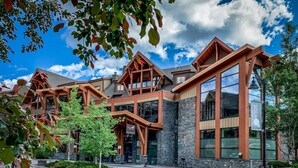 A modern building with a stone facade and large windows, featuring a prominent entrance with a covered porch. - Superb 2BR Condo w/ Charming Mountain View & Pool (Canmore)