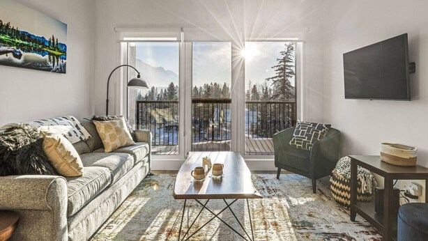 Uma sala de estar moderna com sofá, poltrona e mesa de centro. Possui uma janela grande com vista para uma paisagem nevada.