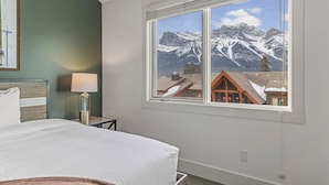 Un dormitorio con cama, mesita de noche, lámpara y ventana con vistas a la montaña.