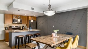 A modern kitchen with wooden cabinets, a central island, bar stools, and a dining table with yellow chairs.