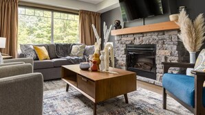 A modern living room with a stone fireplace, a sofa set, and a flat-screen TV mounted above the fireplace.