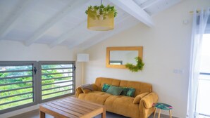 Una habitación con sofá, una mesa de madera, un espejo y una ventana con vistas a zonas verdes.