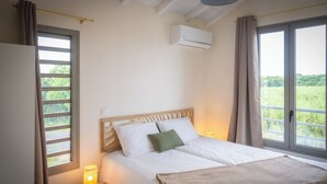 Un dormitorio con cama, una mesita de noche con lámpara, una ventana con cortinas y un equipo de aire acondicionado.