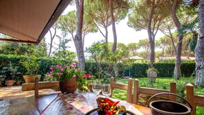 Un espace extérieur aménagé pour prendre les repas, avec une table dressée pour deux personnes, entouré de plantes en pot et d’une clôture en bois.