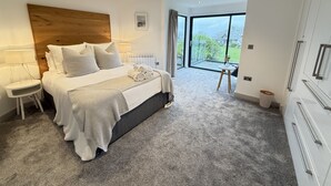 A modern bedroom with a large bed, bedside tables, a view of the outdoors through a large window, and a wooden headboard. - Fishers View - a lodge that sleeps 10 guests in 5 bedrooms (St Ives)