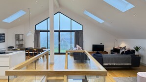 A spacious loft apartment with a high ceiling, skylights, a dining area, a living room with a sofa and TV, and a staircase with glass railings. - Fishers View - a lodge that sleeps 10 guests in 5 bedrooms (St Ives)