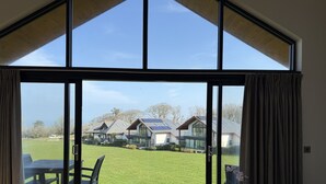 A spacious room with a large sliding glass door leading to a deck. The room features a wooden floor, a small round table with a chair, and a potted plant. - Fishers View - a lodge that sleeps 10 guests in 5 bedrooms (St Ives)