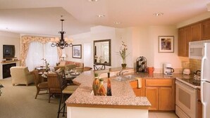 A modern kitchen with granite countertops, a central island, and a dining area with a chandelier.